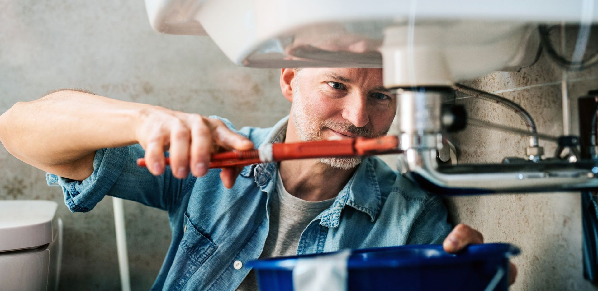 Man trying to fix a leak in a sink using a pipe wrench Man trying to fix a leak in a sink using a pipe wrench