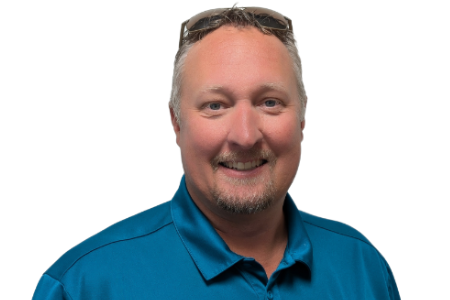 A smiling person with a goatee, wearing sunglasses on their head and a blue polo shirt, set against a white background.