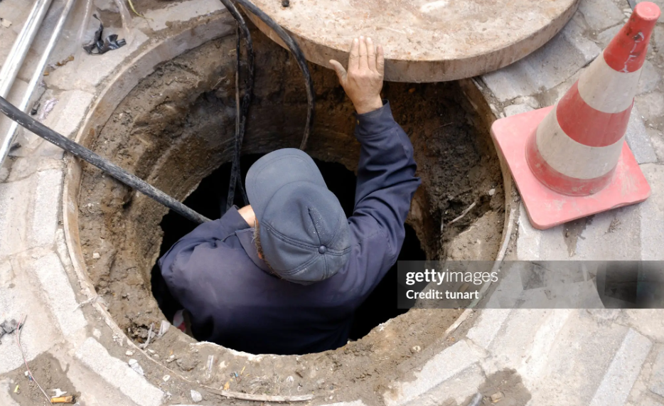 A man in a hole repairing a drain as part of essential emergency sewer cleaning work. A man in a hole repairing a drain as part of essential emergency sewer cleaning work.