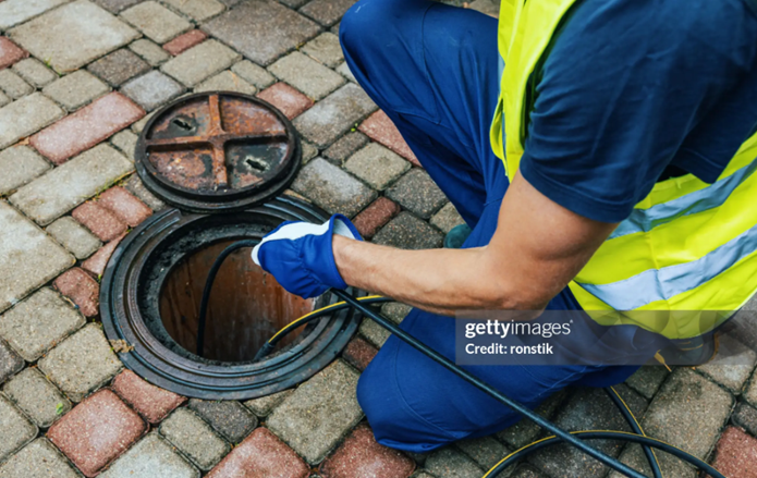 A man in a safety vest repairing a drain as part of essential emergency sewer cleaning work. A man in a safety vest repairing a drain as part of essential emergency sewer cleaning work.