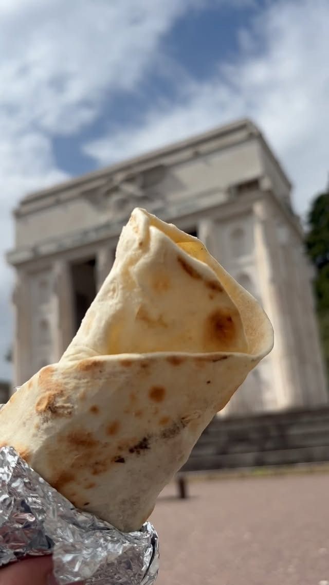Primo piano di una tortilla avvolta davanti a un edificio bianco con colonne in una giornata nuvolosa.
