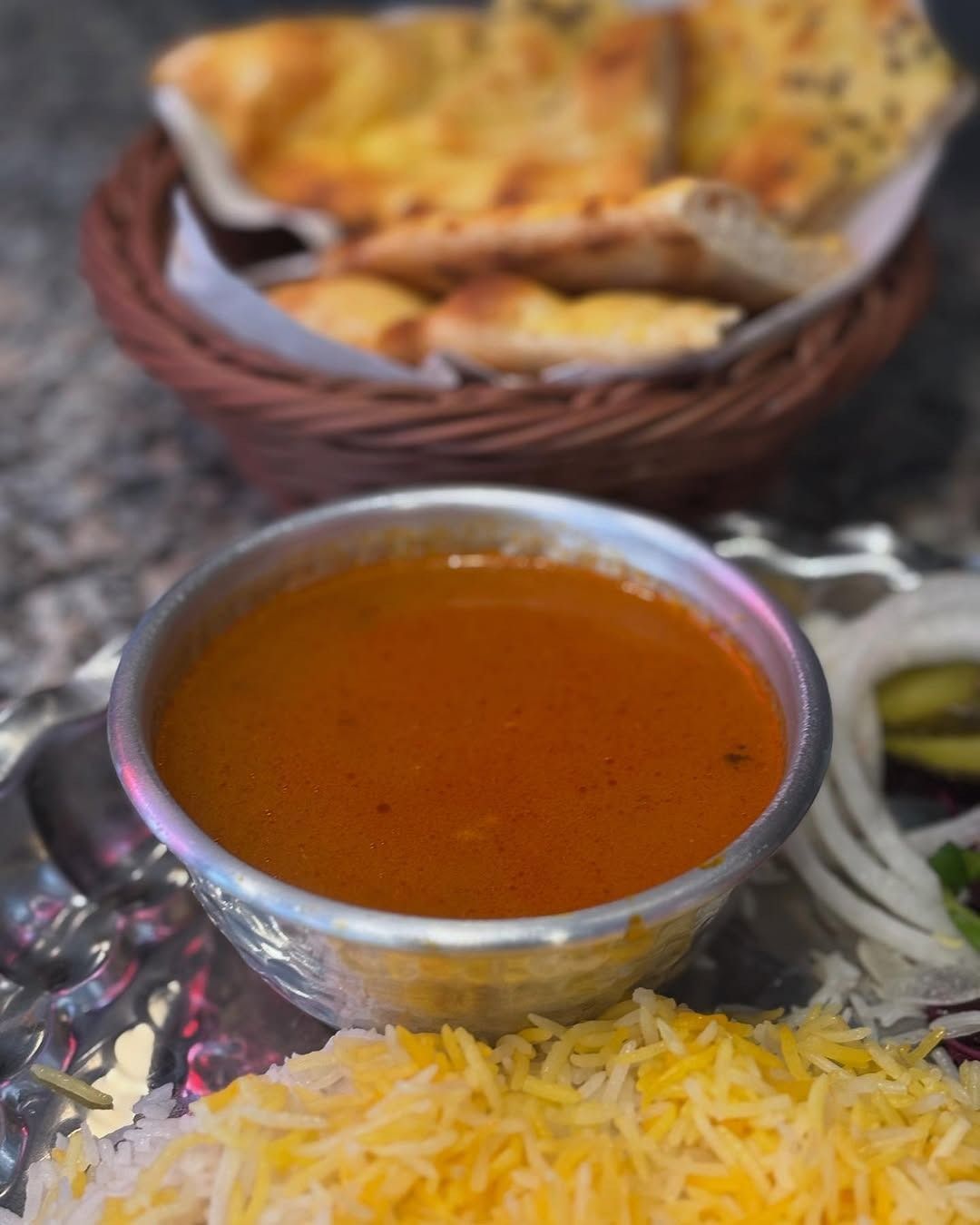 Ciotola di salsa all'arancia, riso, pane naan e una porzione di cipolle.