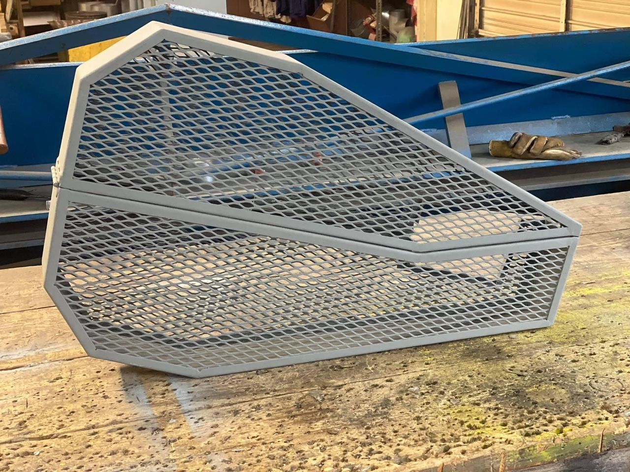 a metal cage is sitting on the ground in front of a blue boat