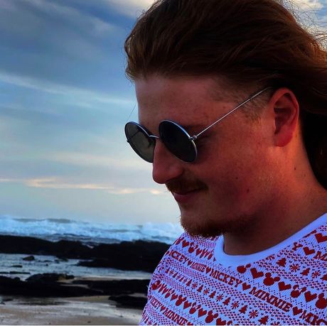 Person in sunglasses on a windy beach with waves and cloudy sky behind them