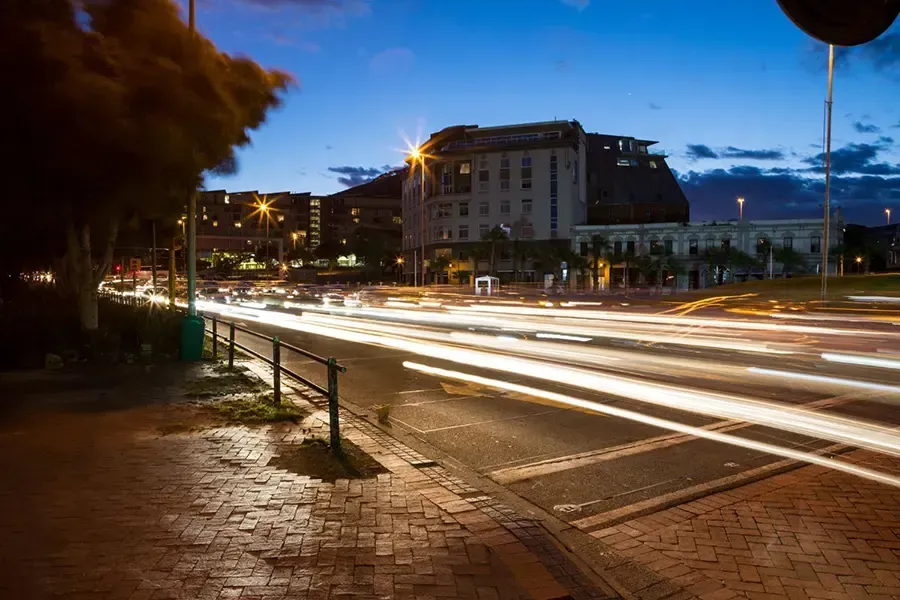 Night city street with light trails from passing cars beside buildings and a wet brick sidewalk