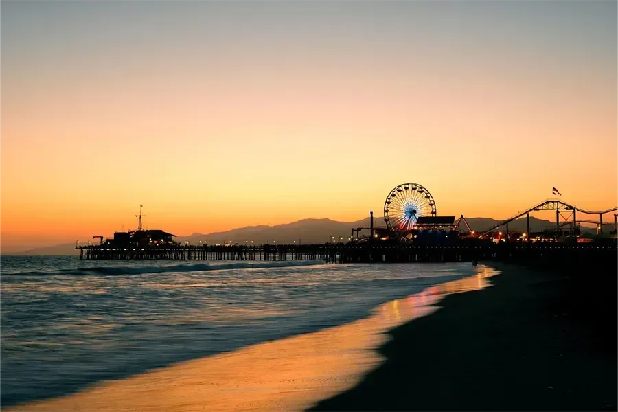 Sunset over a beach with a lit pier and Ferris wheel along the shoreline