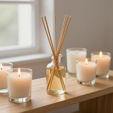 Velas encendidas y un difusor de varillas en una estantería de madera junto a una ventana