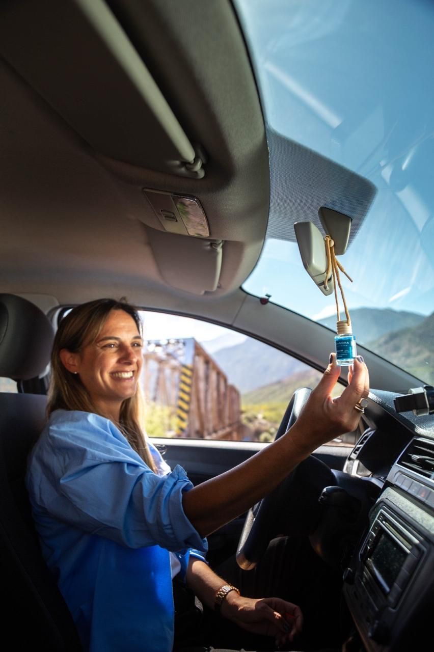 Conductor sonriente mientras sostiene una botella frente al espejo retrovisor dentro de un coche