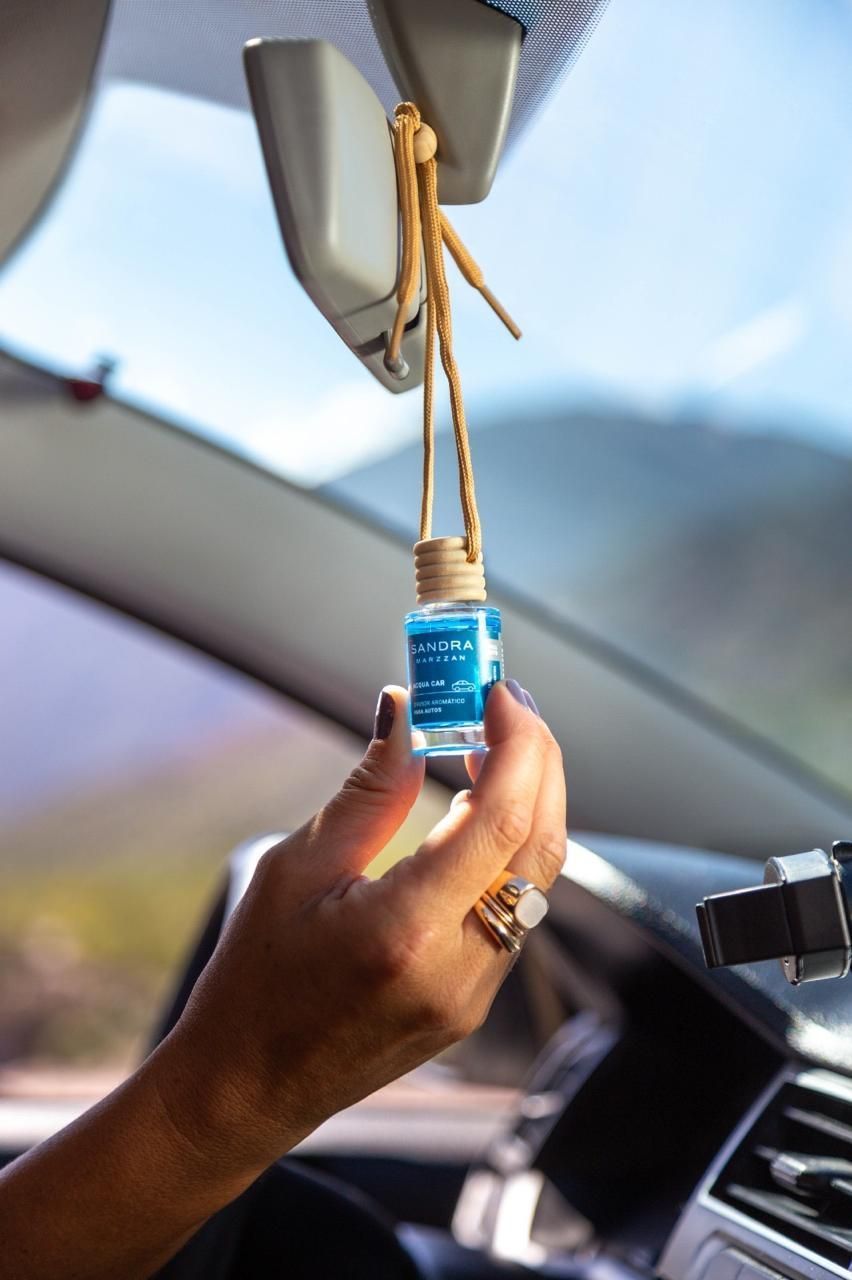 Una mano sostiene una pequeña botella azul con un colgante de cuerda, dentro de un coche