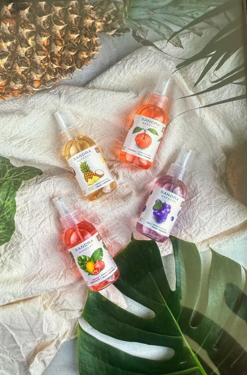 Cuatro bálsamos labiales de colores y aroma frutal sobre una tela blanca, con hojas verdes y una piña
