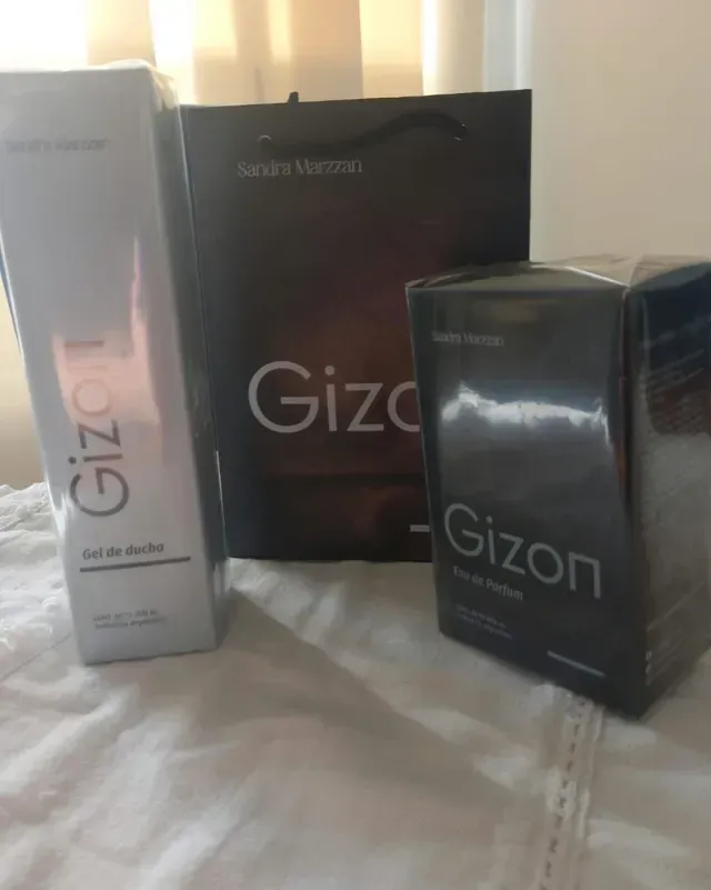 Tres cajas de perfume Gizon en plateado, negro y marrón oscuro sobre una cama blanca