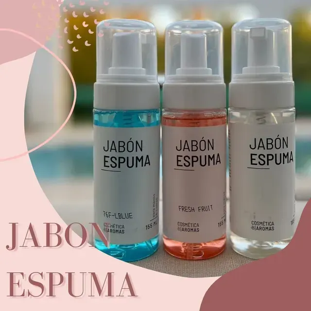 Tres jabones espumosos en dispensadores rosa, azul y transparente sobre un fondo rosado.