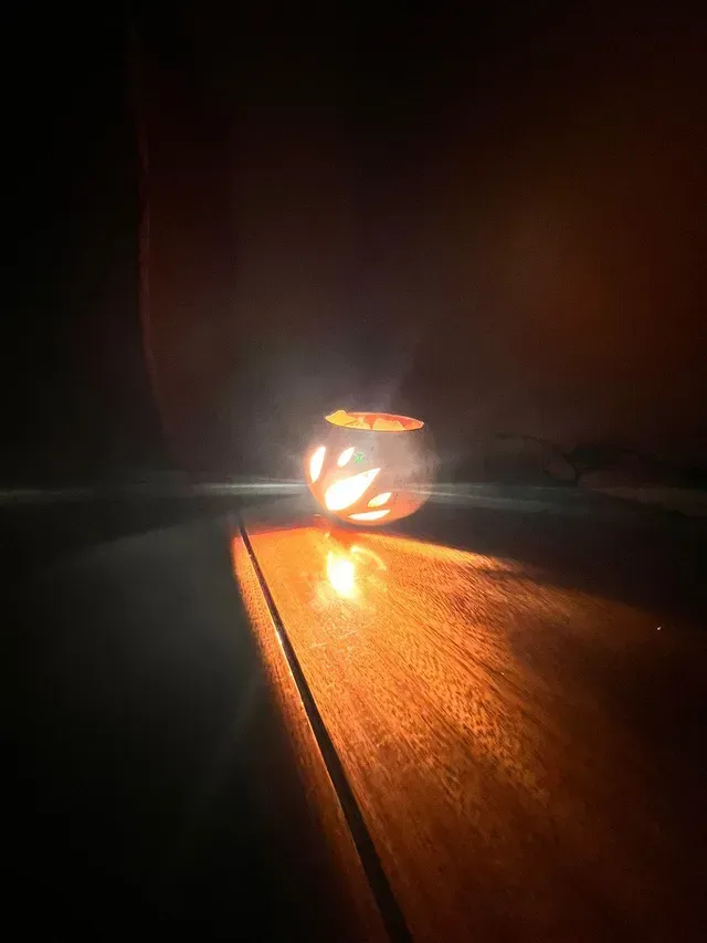 Un pequeño portavelas resplandece sobre una mesa de madera en una habitación oscura, proyectando una cálida luz anaranjada.