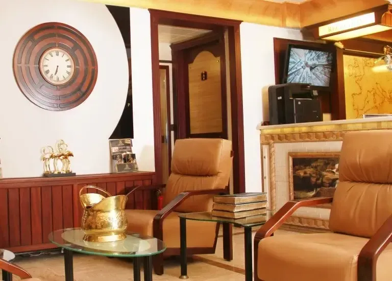 A waiting area with two tan leather chairs, a glass coffee table, a brass bucket, and a large wall clock.
