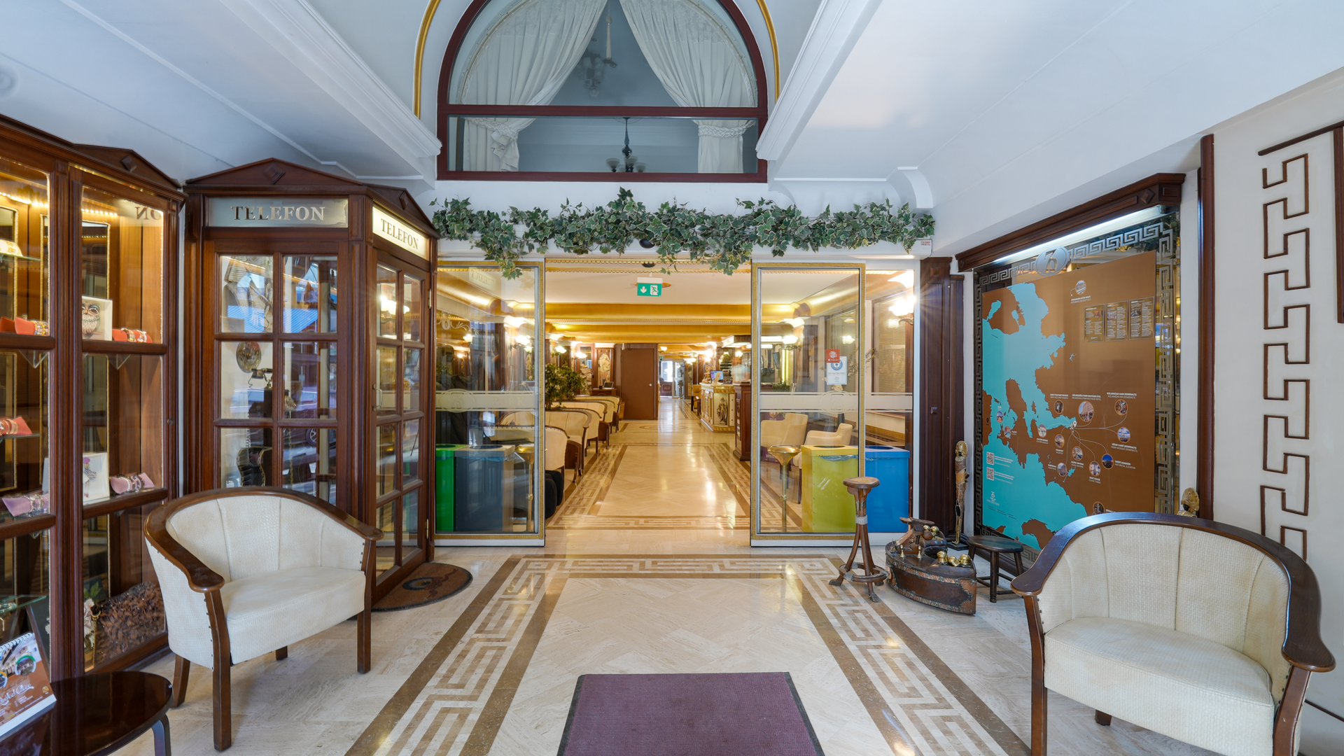 Oğlakçıoğlu İzmir Park Hotel lobby with two armchairs, a wooden phone booth, and a glass-walled entrance to a dining area.