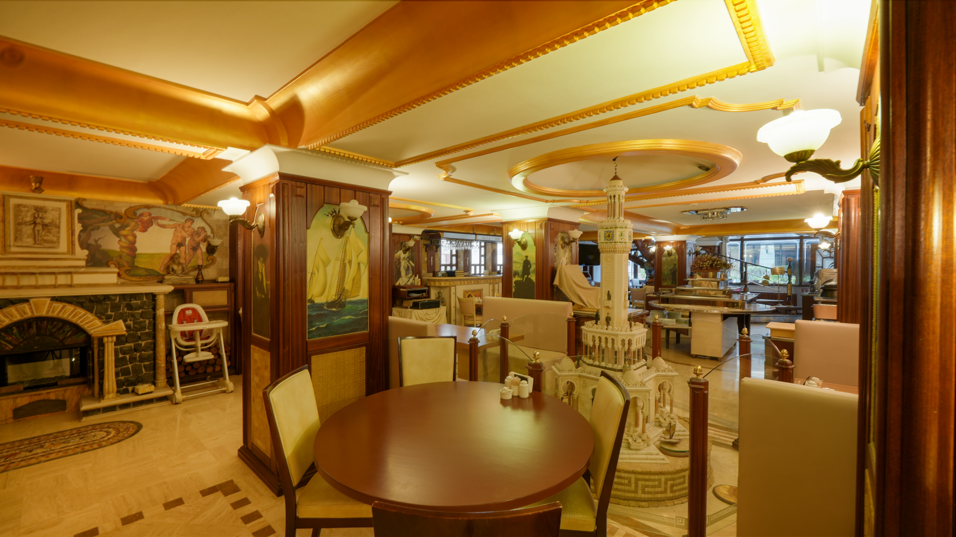 A warmly lit, elegantly decorated restaurant interior featuring round tables, beige upholstered chairs, and wood trim.