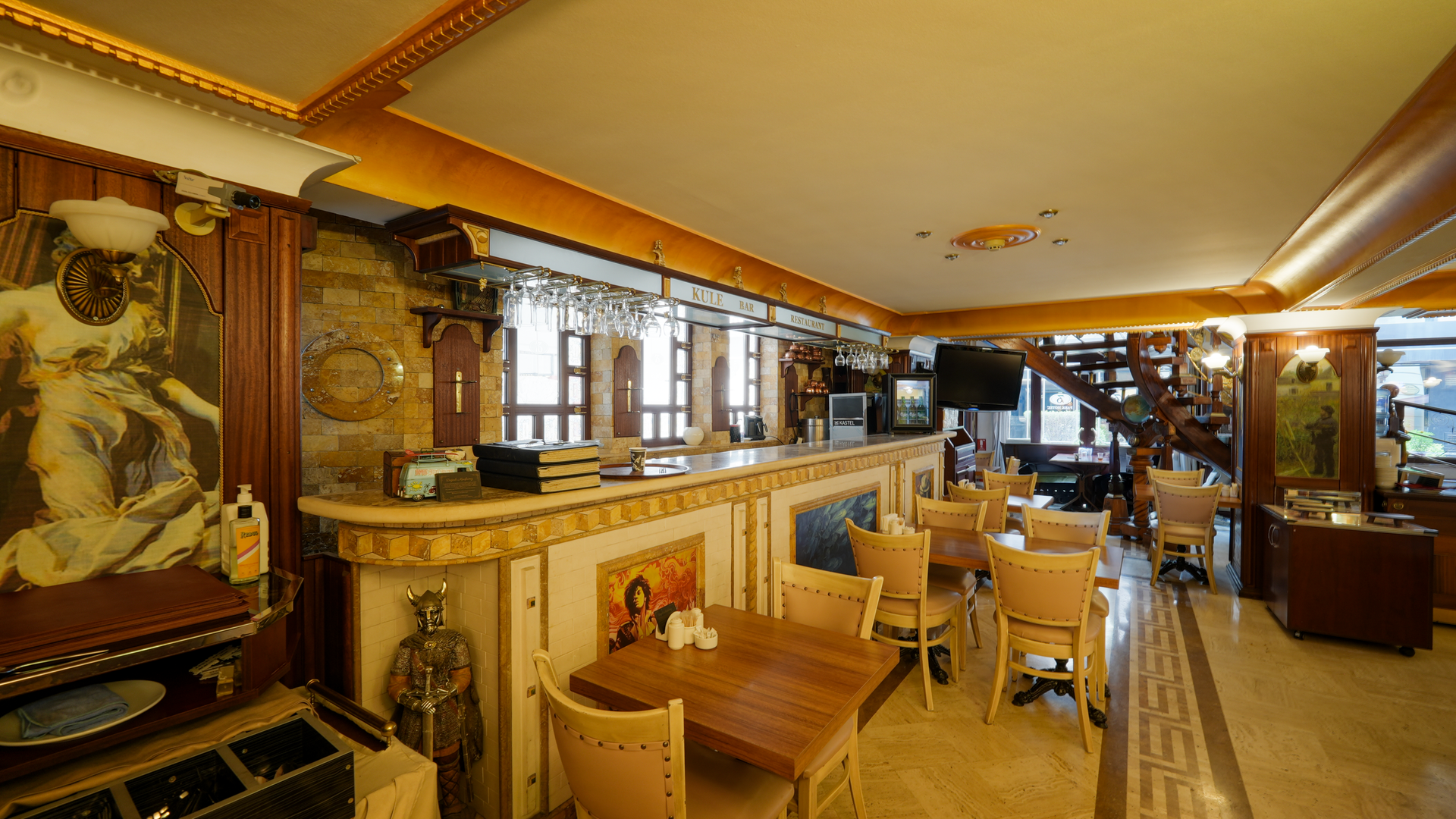 A bar area with wooden tables, beige chairs, warm lighting, and decorative wall art in a restaurant setting.