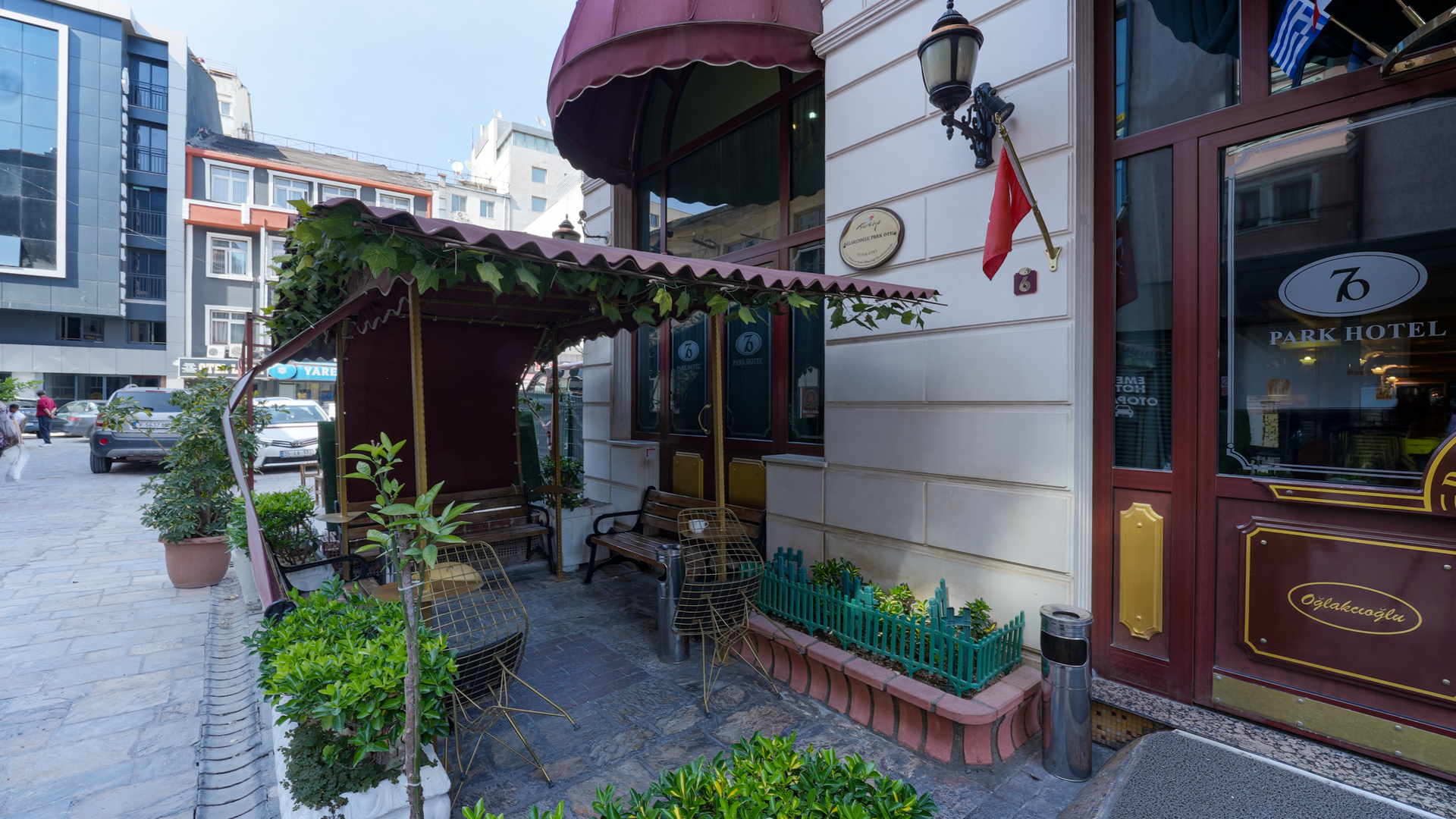 An outdoor seating area for the İzmir Park Hotel, featuring a canopy, potted plants, and a brick-paved sidewalk in İzmir.