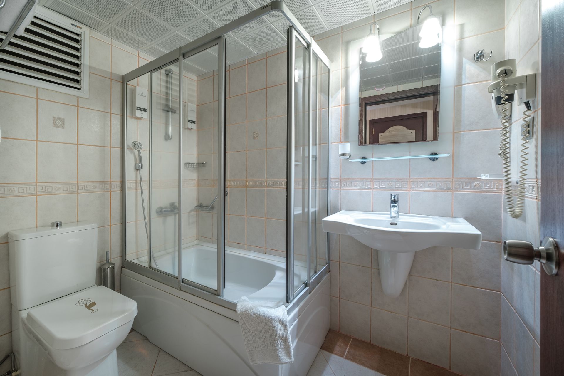 Park Hotel's bathroom with a white toilet, a bathtub behind a glass enclosure, and a wall-mounted sink with a mirror above.