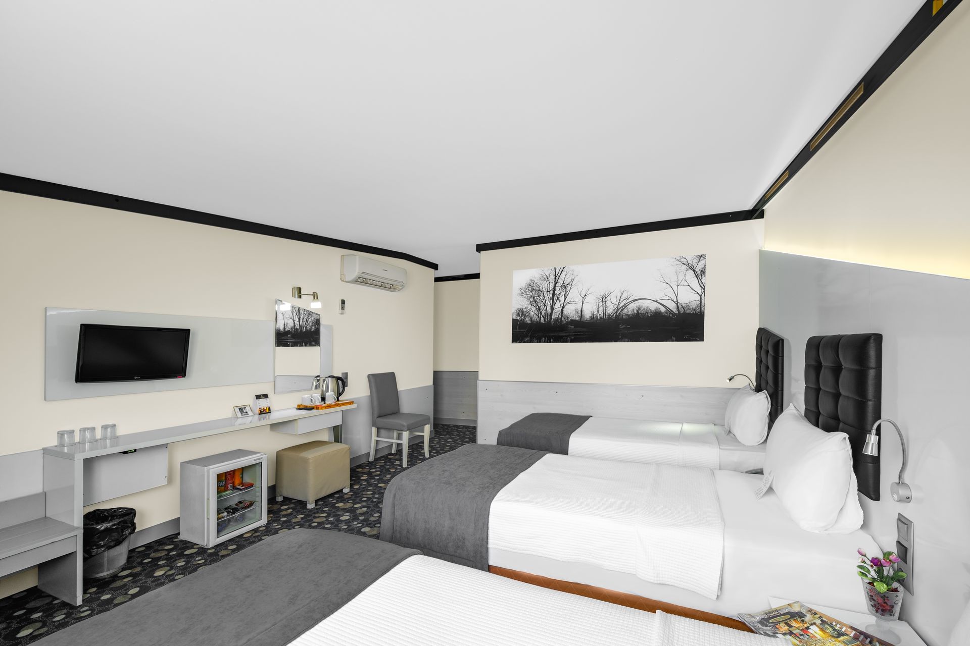 İzmir Park Hotel's room with three beds featuring white linens and gray accents, a wall-mounted TV, and a mini-fridge.