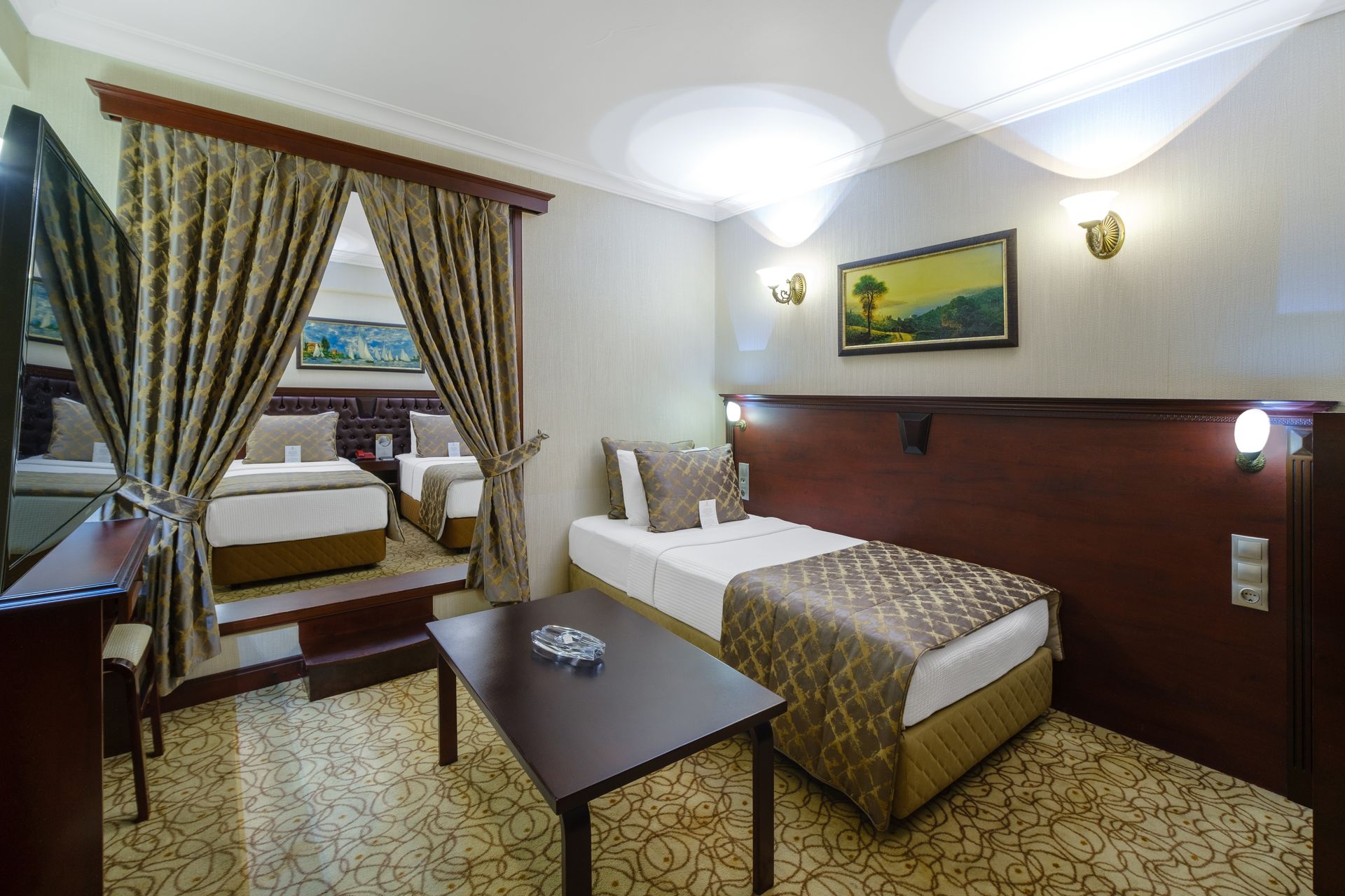 İzmir Park Hotel's modern room with two beds, one separated by curtains, a small coffee table, and warm wall lighting.
