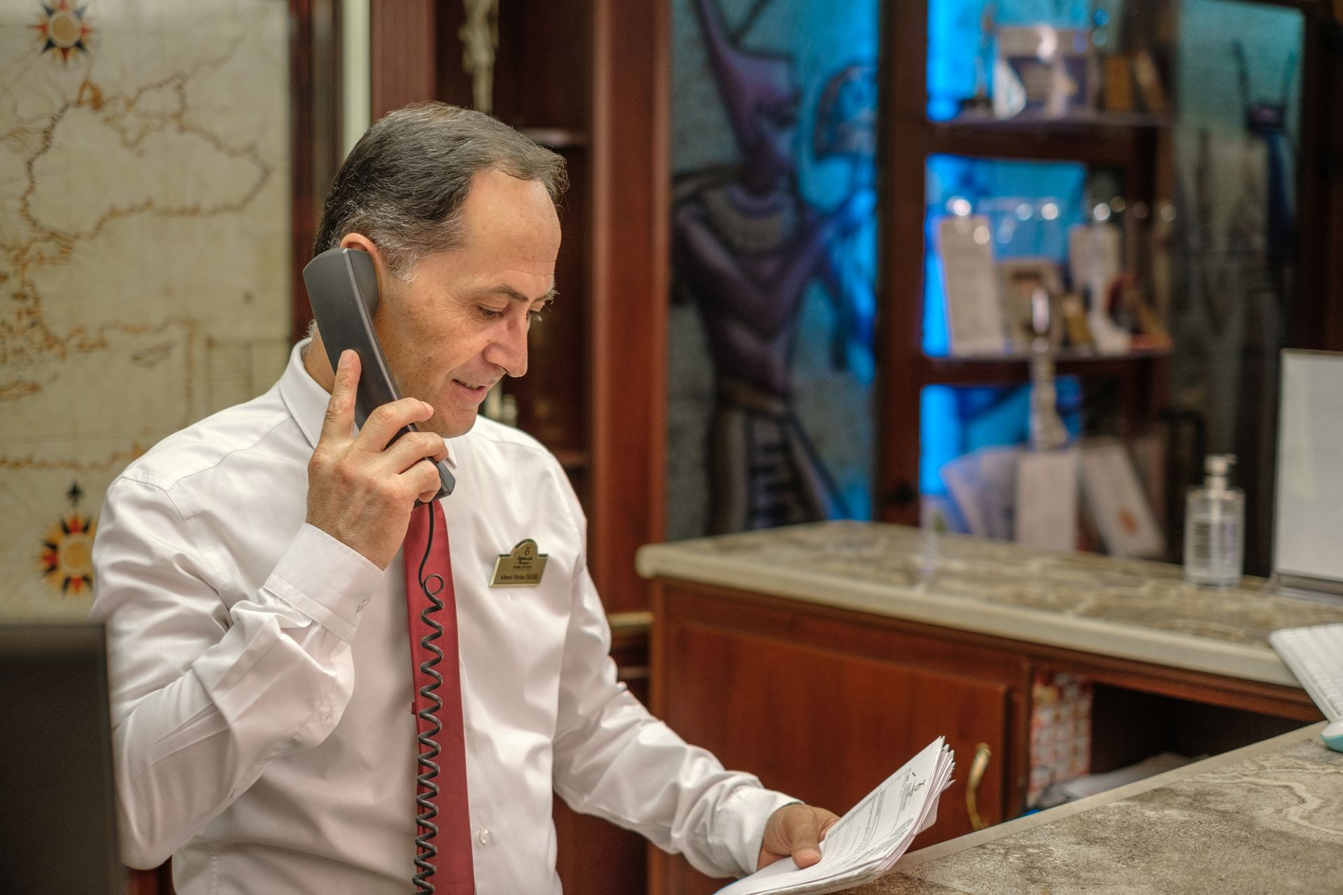 Oğlakçıoğlu İzmir Park Hotel's professional at a hotel front desk talks on a landline phone while holding a document.