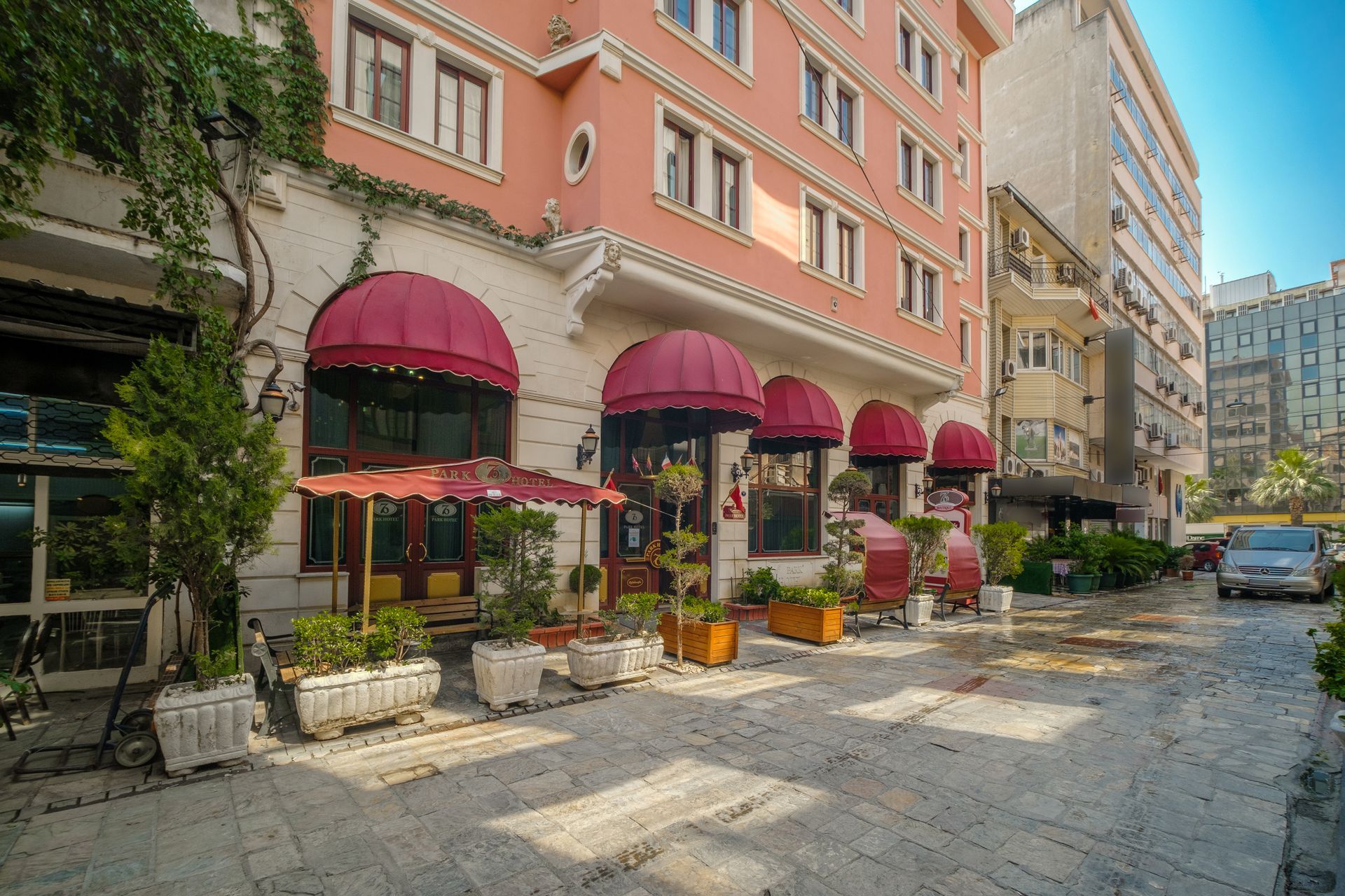Oğlakçıoğlu İzmir Park Hotel building with red awnings over storefronts along a cobblestone sidewalk.