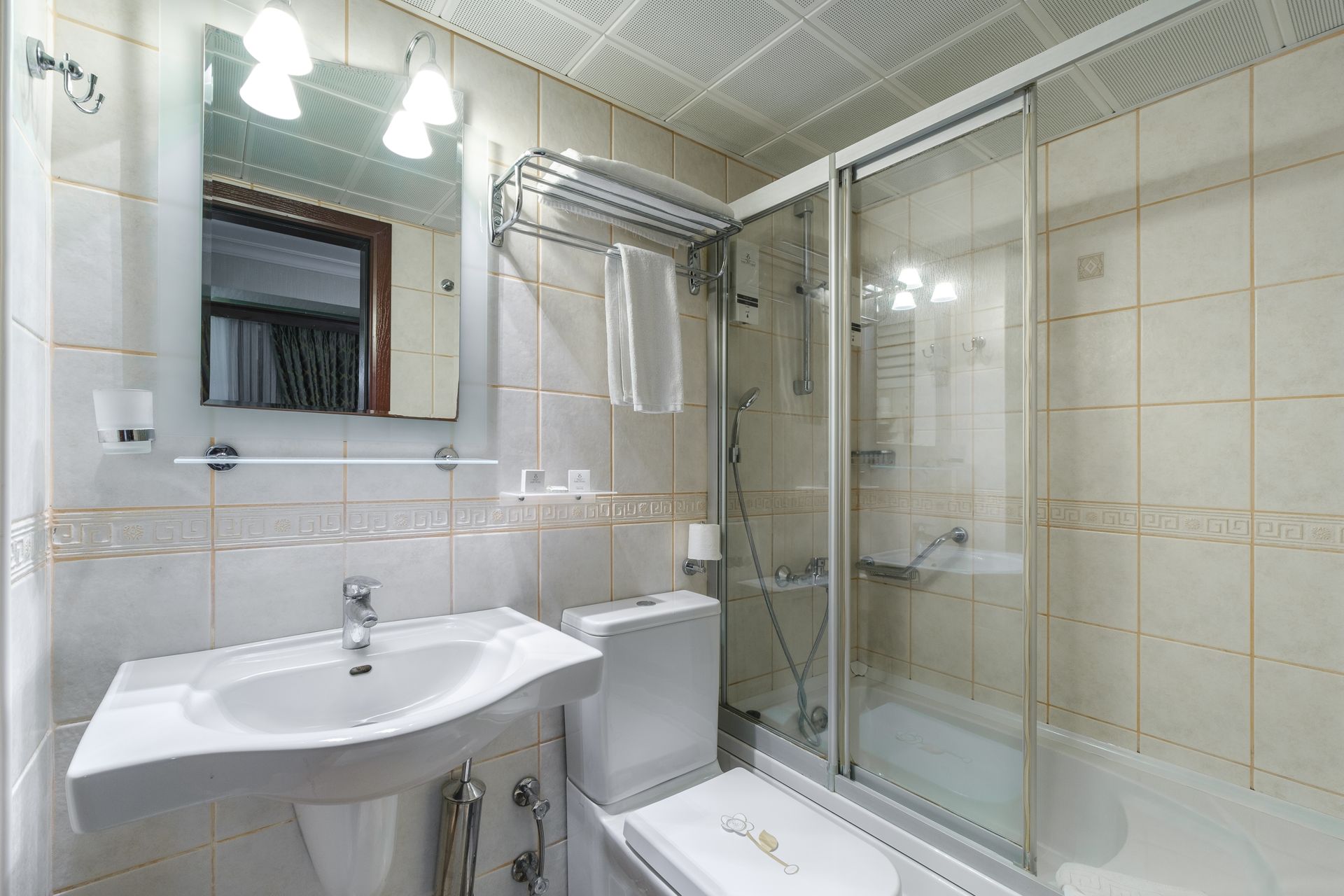 İzmir Park Hotel's bathroom featuring a white pedestal sink, a toilet, a shower with a glass door, and a wall-mounted mirror.