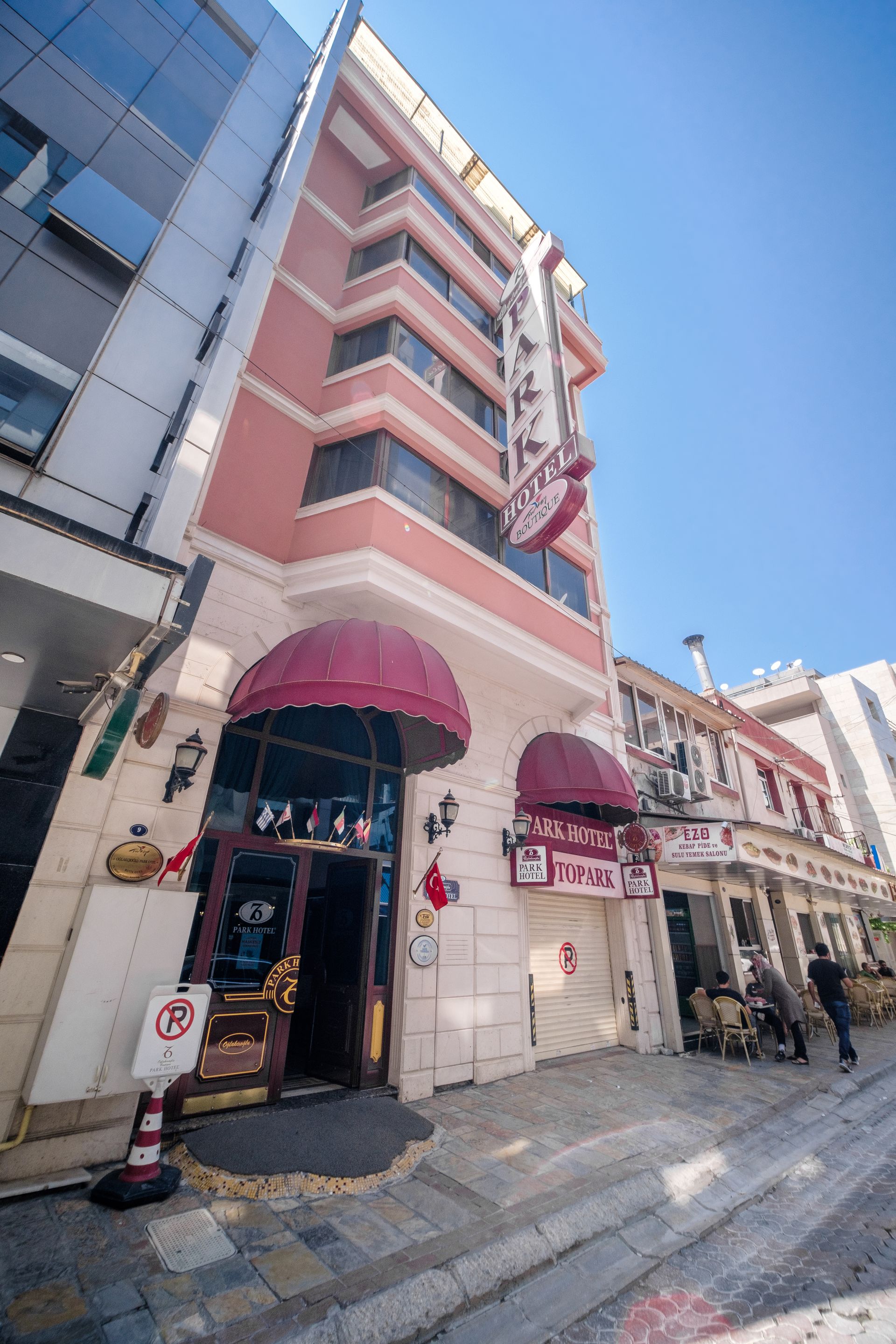 İzmir Park Hotel building with a peach facade, red awnings over entrances, and a prominent vertical sign on a street.