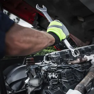 Mechanic with wrench working on a truck engine; wearing safety gloves.