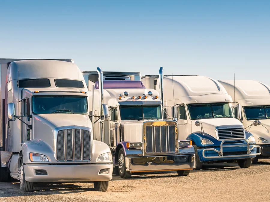 A row of semi trucks are parked in a parking lot.