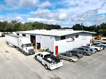 A warehouse with trucks and cars parked in front of it.