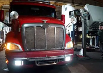 Red semi-truck in a garage with headlights on, seen from the front.