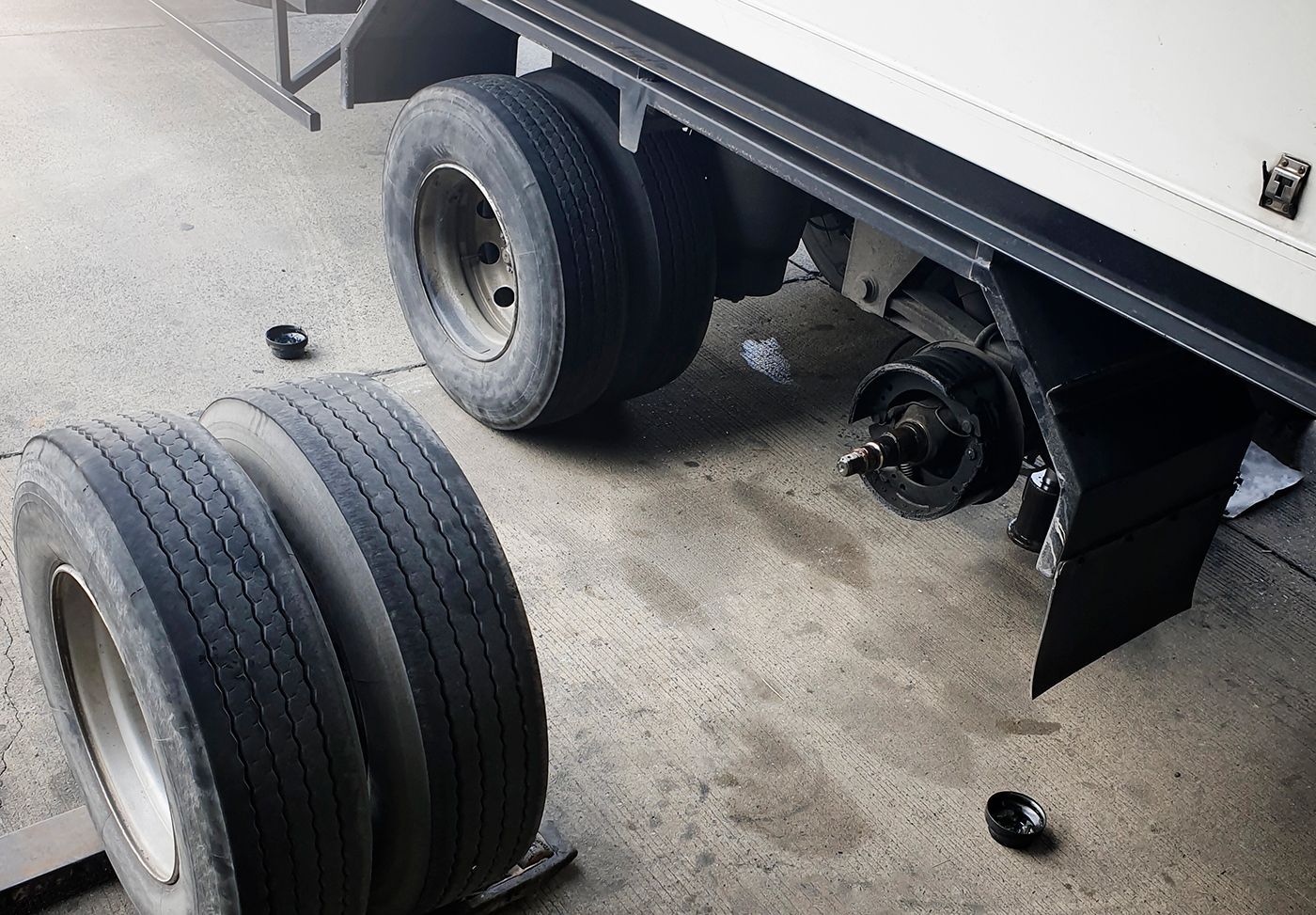 A truck with a broken wheel is sitting in a garage next to a stack of tires.