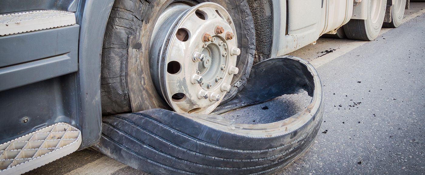 A semi-truck with a flat tire on the side of a road.