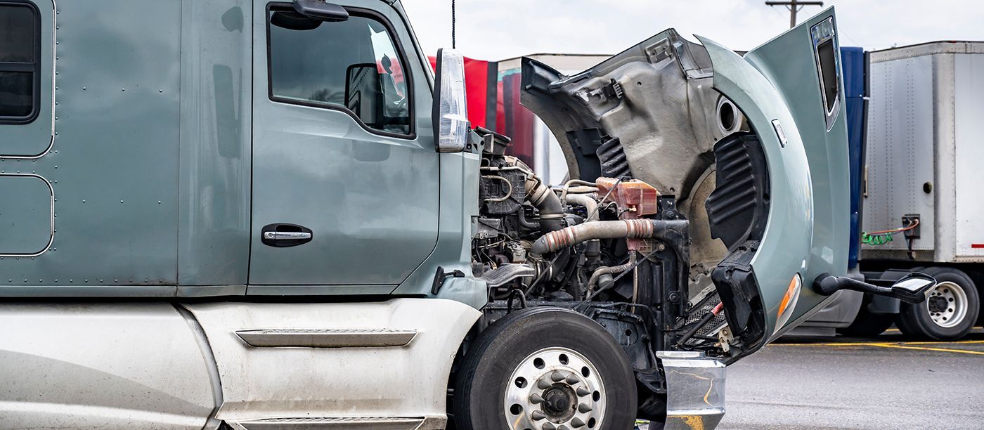 Semi-truck with hood open, parked in a lot. Engine is visible. Another trailer is in the background.