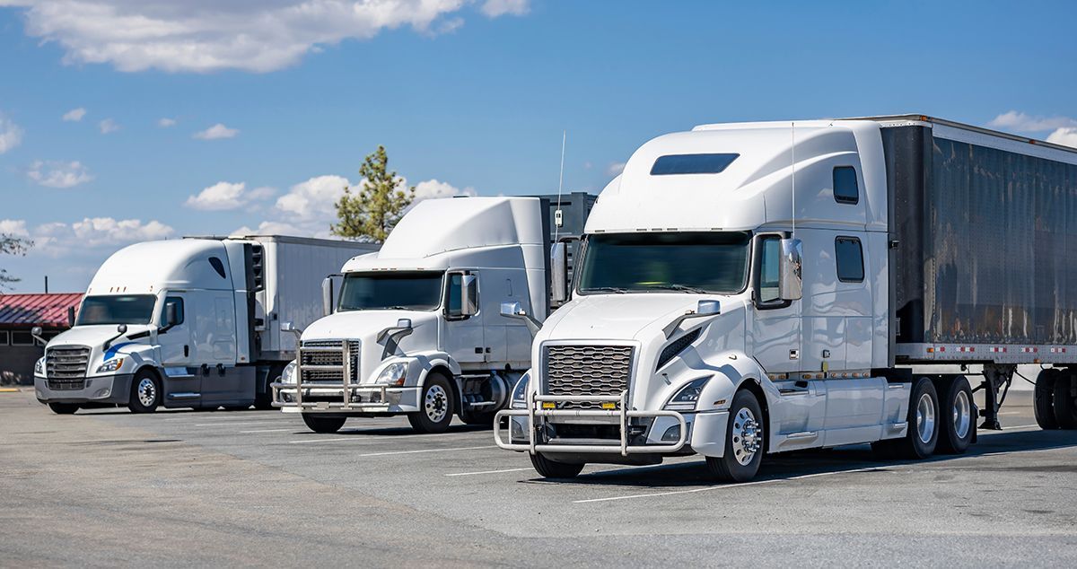 Three white semi-trucks parked outdoors under a blue sky.