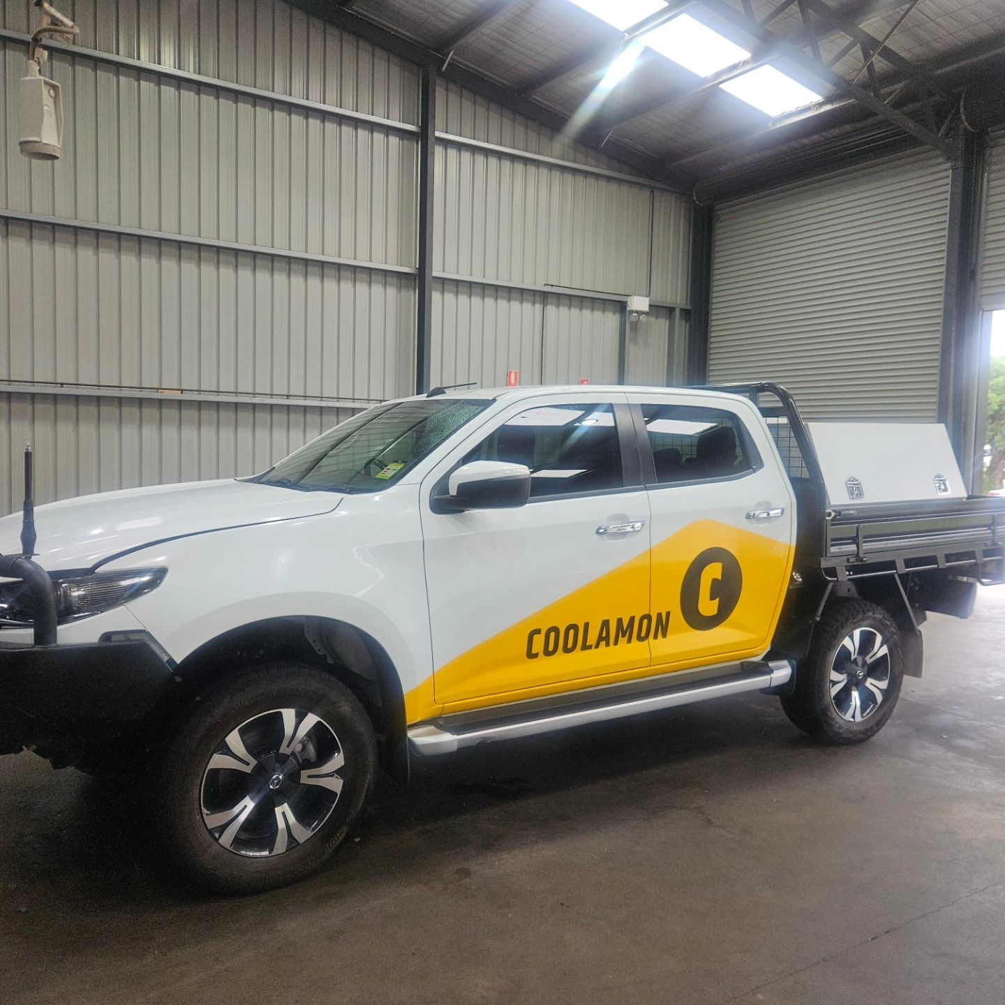 White Coolamon utility pickup truck parked inside a warehouse, with yellow side branding and trailer attached — On Point Detailing Wagga in East Wagga Wagga, NSW