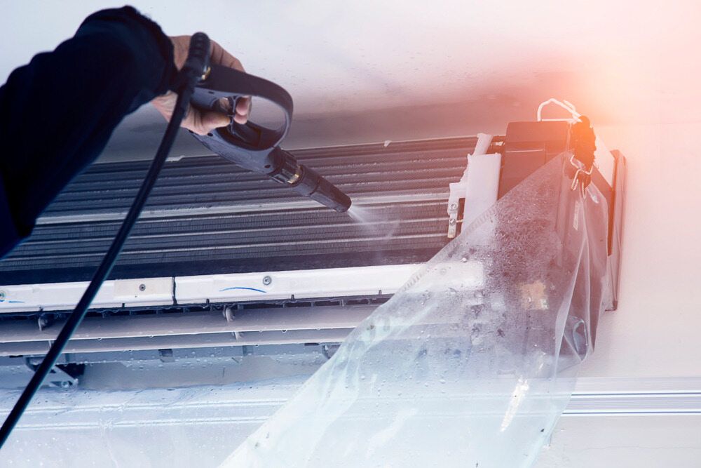 Person Cleaning an Air Conditioner With a Spray Gun — Hinterland Air Conditioning Sunshine Coast in Palmwoods, QLD