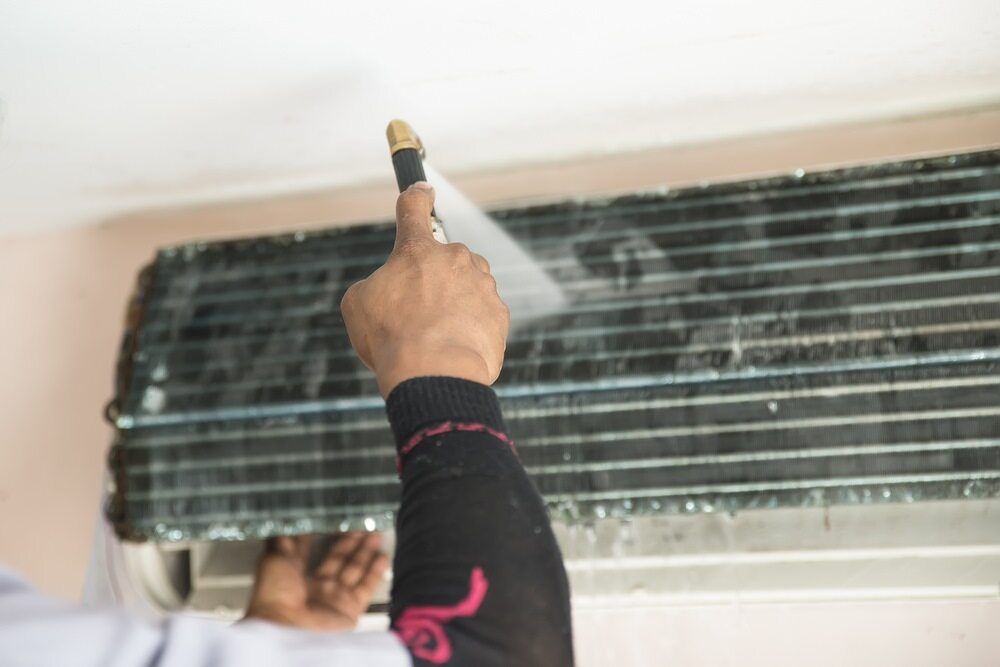 Person Cleaning an Air Conditioner With a Spray Nozzle — Hinterland Air Conditioning Sunshine Coast in Palmwoods, QLD