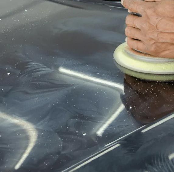 Hand polishing a dark car hood with a buffer, removing swirl marks
