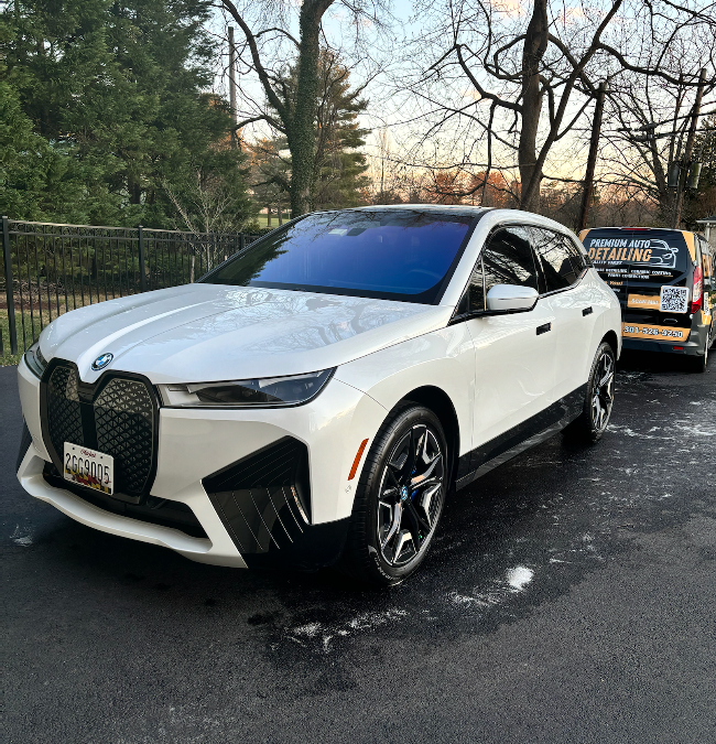 White BMW SUV parked on a snowy driveway beside a fence and trees