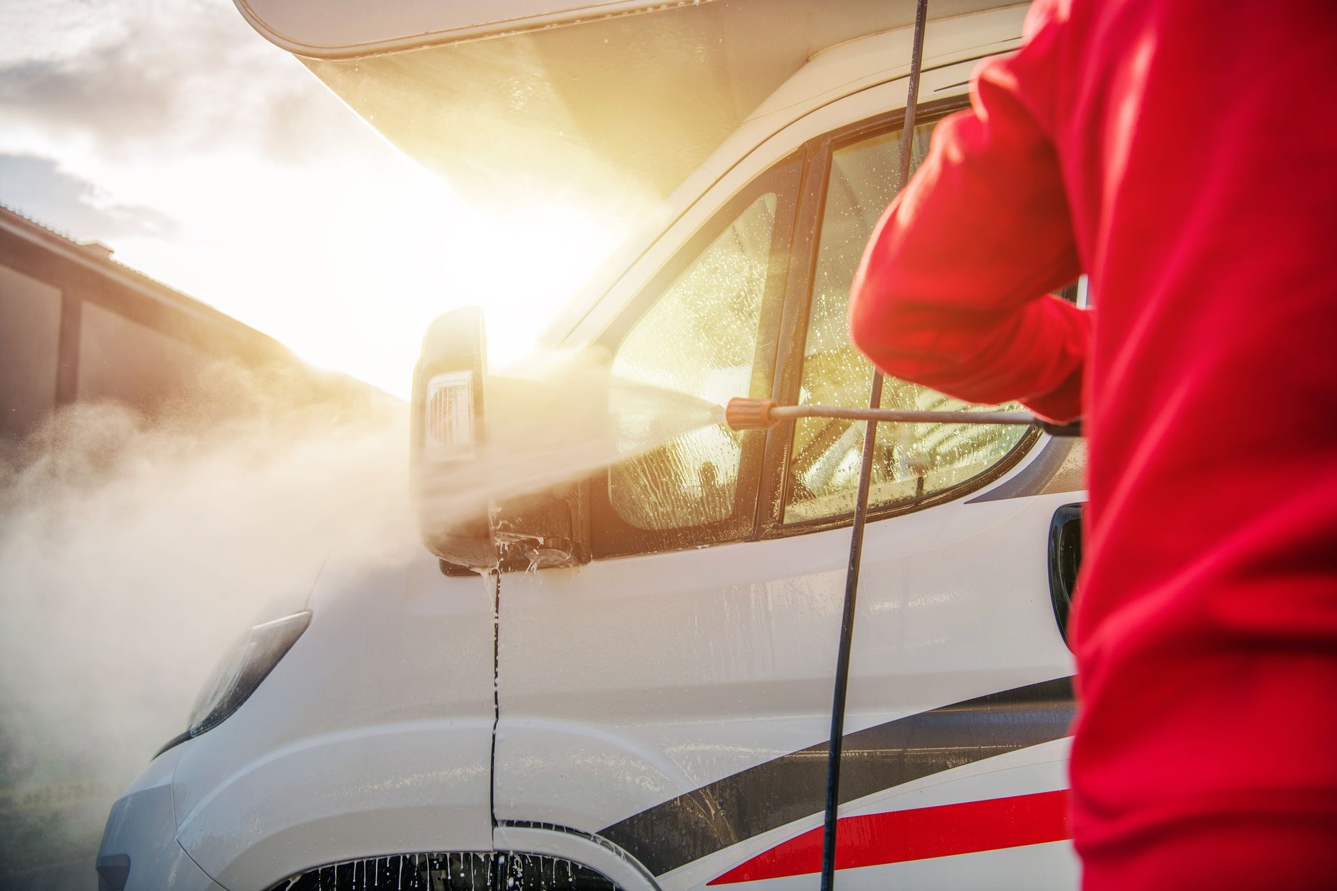 Person pressure-washing a white van with sunlight and spray mist