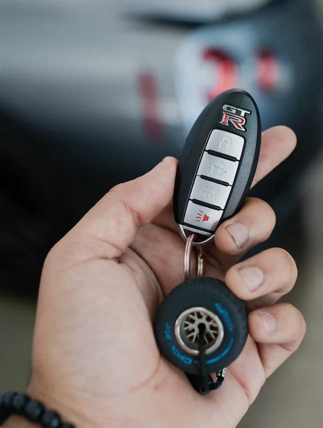 Hand holding a black-and-blue car key fob and key, with a blurred car in the background