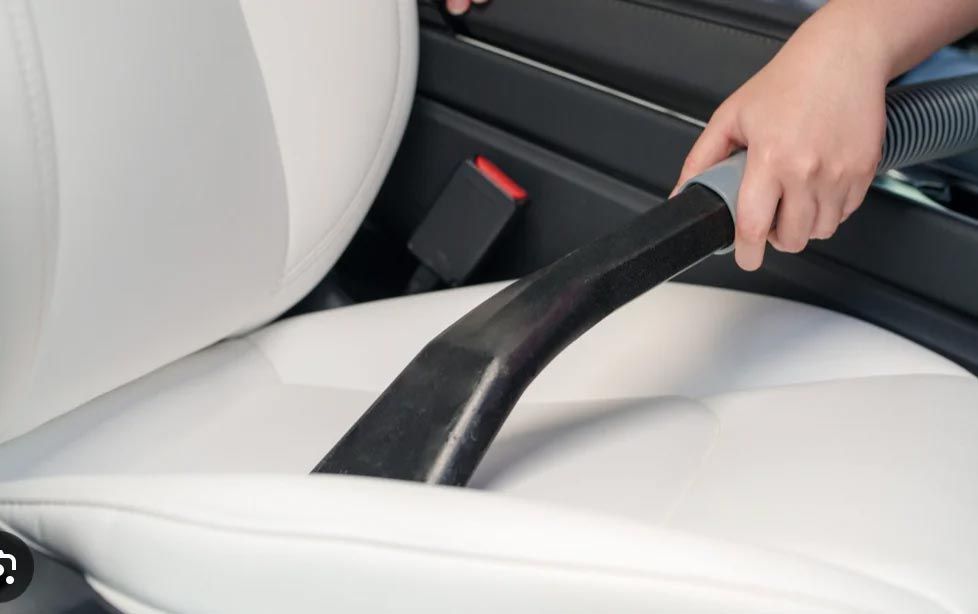Hand using a handheld vacuum to clean a white car seat interior