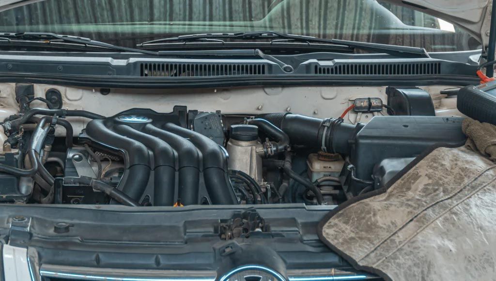 Car engine bay with exposed black intake manifold and a dusty cloth covering part of the right side.