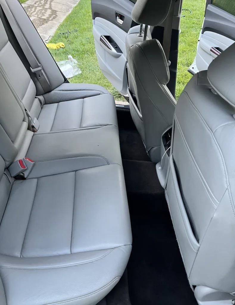 Car interior with gray leather rear seats and open doors, showing the back seat area.