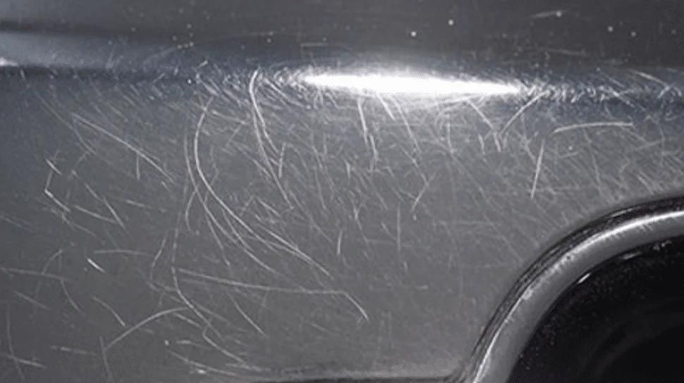 Close-up of a dark car panel with many scratch marks and a bright reflection near the top
