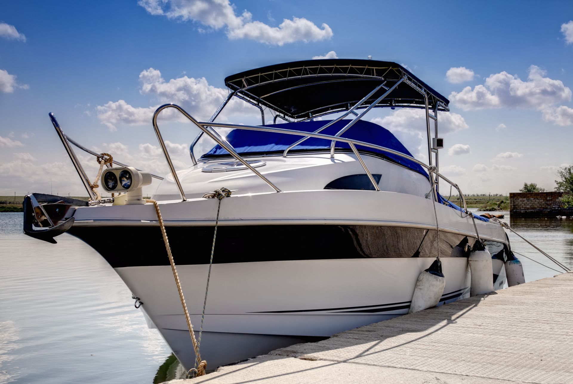White and blue motorboat docked at a marina on calm water under a partly cloudy sky