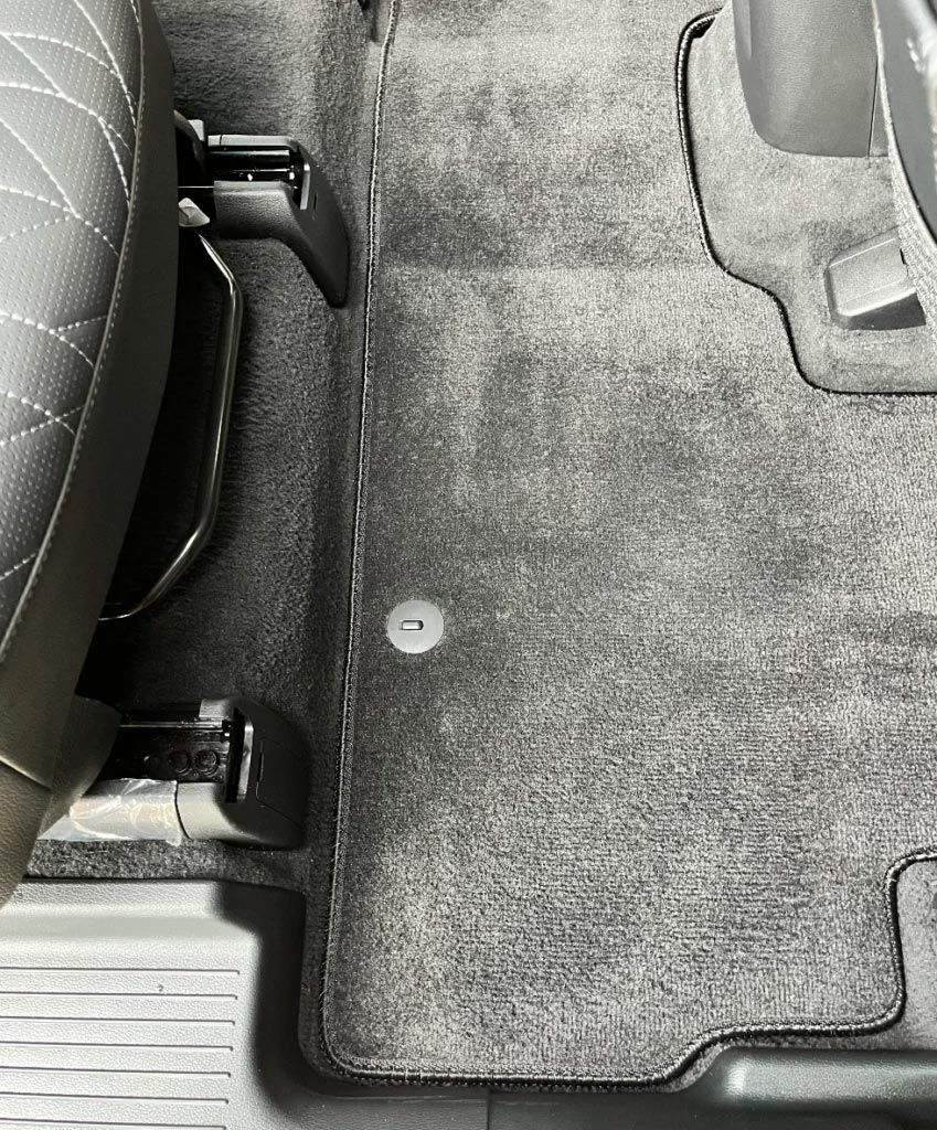 Car floor mat beneath a black seat with visible mounting hardware